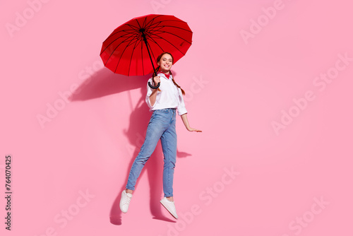 Full length photo of cute sweet lady dressed cowboy outfit jumping high holding parasol emtpy space isolated pink color background