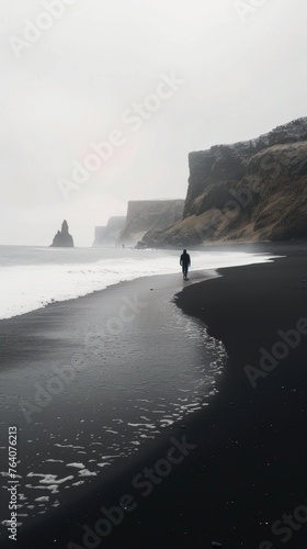 Person walking on black sand beach with misty cliffs in the background