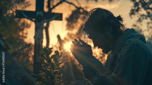 Man kneels next to cross while praying, man kneels in prayer in front of cross.