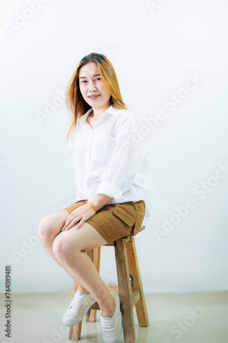 Young Asian woman sitting at a chair, isolated on a white background.Portrait studio cutout shot of Asian young pretty short hair female model in long brown coat jacket casual shoes sitting crossed 