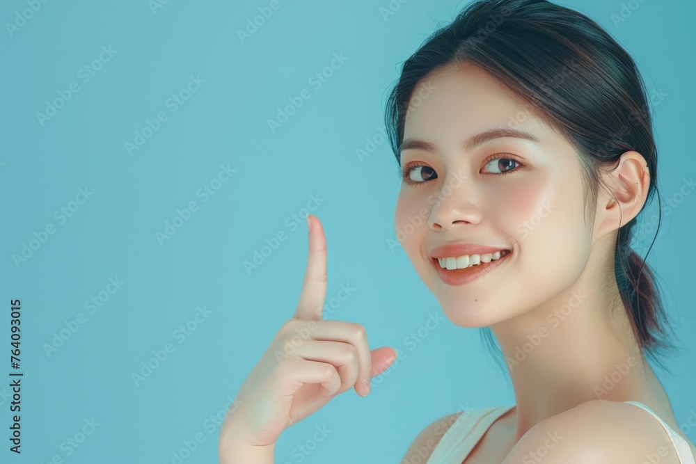 Smiling Asian Beauty Pointing Upwards on Solid Blue Background. Generative AI. Smiling Asian Beauty Pointing Upwards on Solid Blue Background. Generative AI.