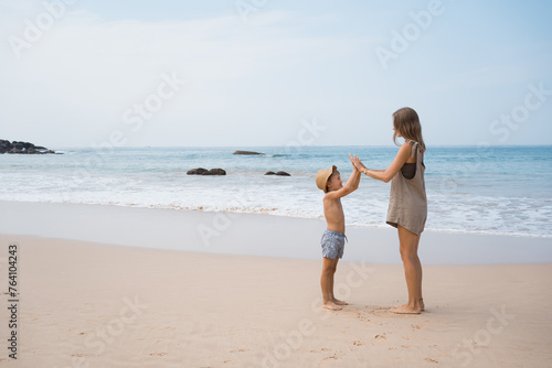 Mother plays with son on beach in summer holidays in tropical country