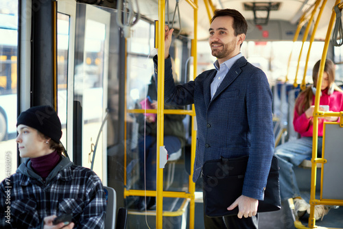Focus on smiling man in jacket using public transport, modern tram for transportation. Blurred people on background. Concept of public transport, urban lifestyle
