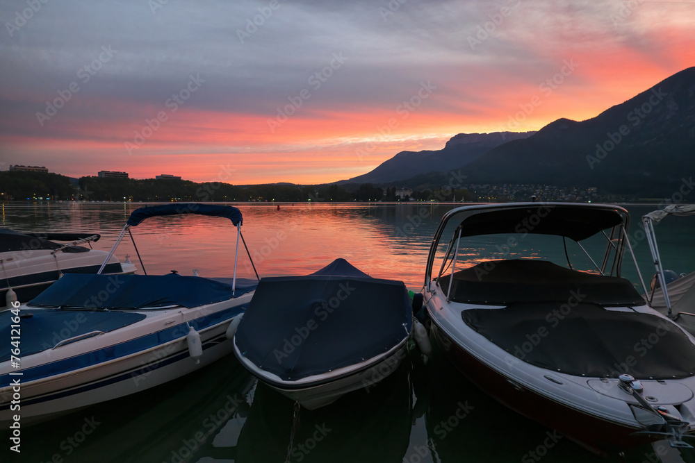 Early morning on Lake Annecy. France. In the foreground there are boats moored, in the background you can see the sunrise over the mountains and the city. Scenery.