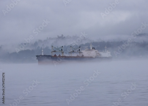 Billede på lærred A lone freighter sailing across fog laden waters with mountains in the background