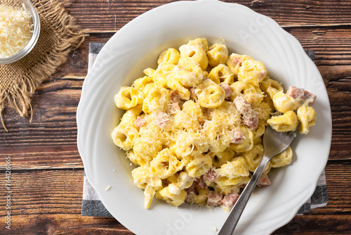 Traditional Italian recipe, Tortellini with ham and cream on a white dish and wooden table.