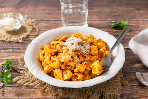 Traditional Italian dish, Tortellini with Bolognese sauce on a white plate and wood background.