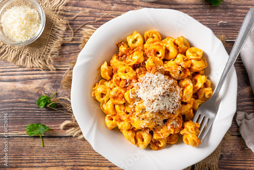 Traditional Italian dish, Tortellini with Bolognese sauce on a white plate and wood background.