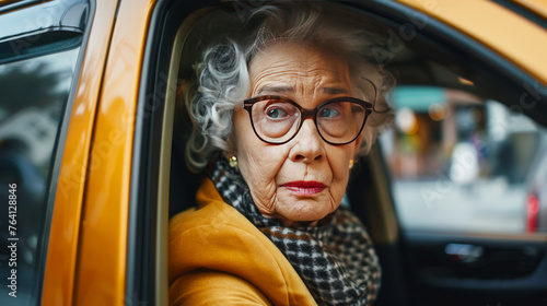 Elderly woman in yellow gazing out from a car window with a thoughtful expression © thanakrit