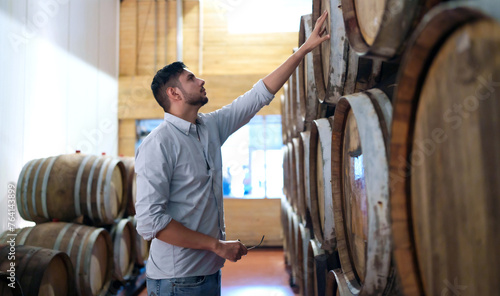 Professional man winemaker working and inspecting wine quality in wine cellar with wooden barrel in wine factory. Winery manufacturing industry, Alcohol and winemaking fermentation process.