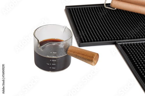 Measuring cup with wooden handle on bar mat over white background.