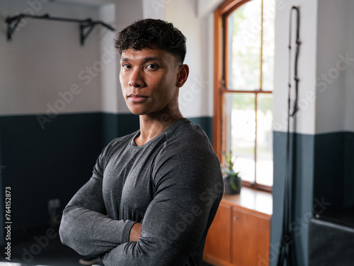 A man stands in the gym, arms crossed, observing the room