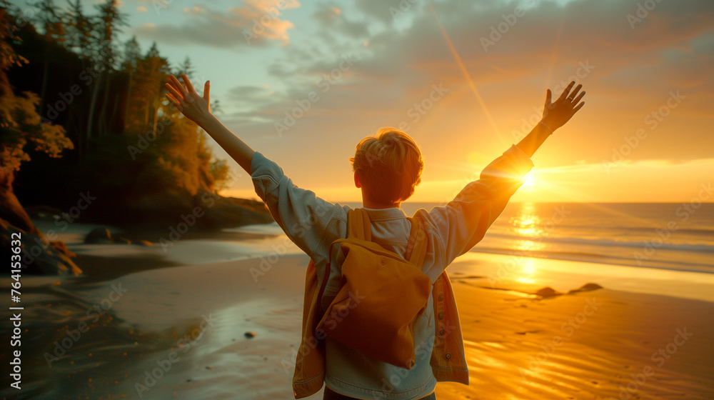 A person raising arms high in celebration facing the sunset on a serene beach - obrazy, fototapety, plakaty 