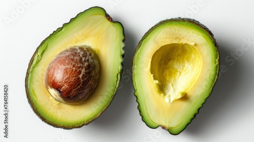 Two halves of a freshly cut avocado with a shiny pit, showing vibrant green flesh and textured skin on a white background. photo