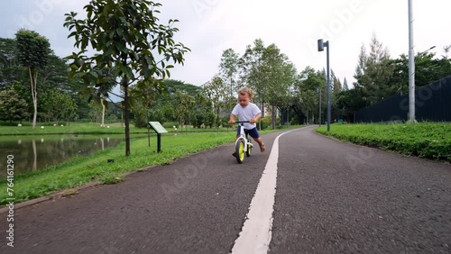 Wallpaper Mural Spirited young child races through verdant park on balance bike, confidently propelling himself forward with each push of his feet. Scene captured in slow motion with reverse dolly shot Torontodigital.ca