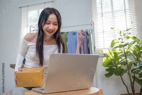 Working Young Asian woman at home selling outfit cloth online internet and using smartphone cellphone laptop to talk communicate chat with customer, Online shopping concept