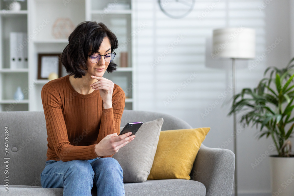 Obraz premium Woman in orange sweater using smartphone on couch