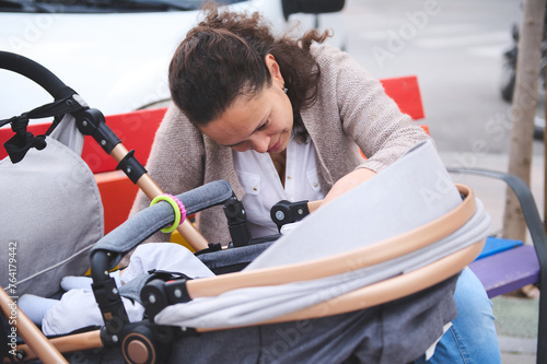 Happy young mother smiling looking at her baby sleeping in baby pram. Maternity leave. Motherhood. Childbirth concept