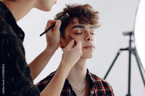 A makeup artist is applying eyeshadow on a young beautiful man Isolated on solid white background