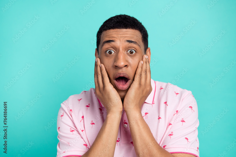 Photo of impressed young man arms touch cheeks open mouth speechless staring isolated on teal color background Photo of impressed young man arms touch cheeks open mouth speechless staring isolated on teal color background