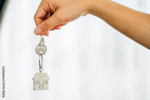 Hand holds key to house marking homeowners' achievement. Agent presents model home symbolizing real estate success. Confidence and happiness resonate.