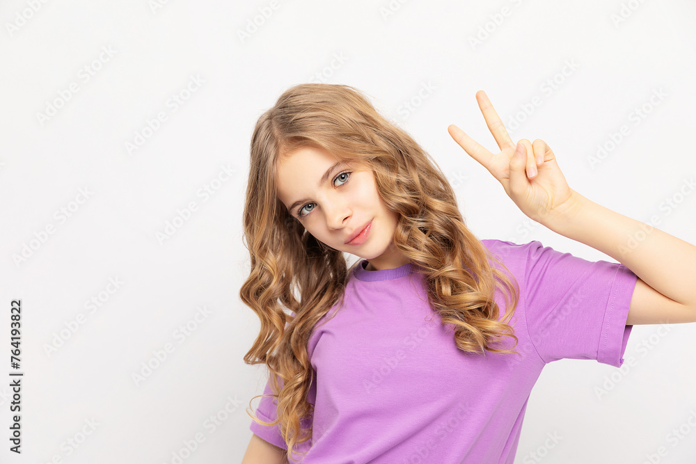 Happy smiling young lovely carefree confident sweet girl with blonde curly hair showing victory sign or peace symbol with fingers, isolated on white background Happy smiling young lovely carefree confident sweet girl with blonde curly hair showing victory sign or peace symbol with fingers, isolated on white background