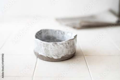An empty ceramic bowl made of gray clay on a white table against a background of a linen napkin. Horizontal orientation.