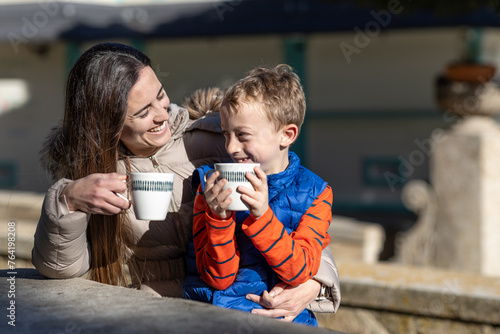 A smiling mother shares hot chocolate with her young son on a picnic area, while they look at each other knowingly. photo