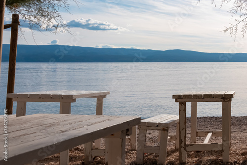 Wooden bench on idyllic beach bar on Plaza Brzet in coastal town Omis  Split-Dalmatia  Croatia  Europe. Adriatic Mediterranean Sea in summer at sunset on Balkans. Vacation concept. Tropical travel