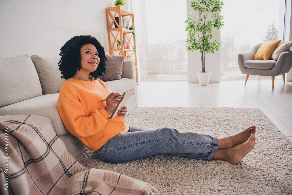 Fototapeta premium Photo portrait of lovely young lady thinking sit floor write notes dressed casual orange clothes cozy day light home interior living room