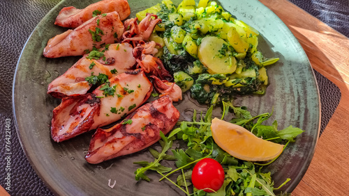 Plate of grilled squid with fresh lemon and potatoes served in local restaurant in coastal village Okrug Gornij, Split-Dalmatia, Croatia, Adriatic Mediterranean Sea, Europe. Local traditional sea food