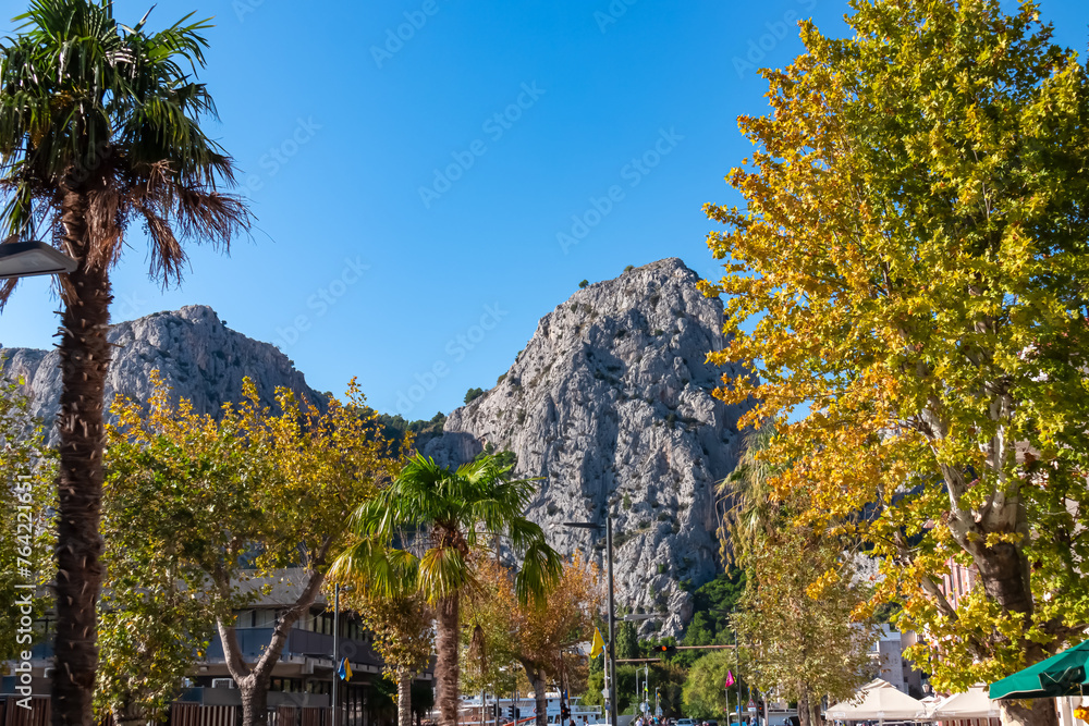 Palm trees along promenade in Omis surrounded by Dinara mountains in Split-Dalmatia, South Croatia, Europe. Majestic coastline of Omis Riviera at Adriatic Sea in Balkans. Travel destination in summer