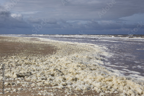 Dutch beach with sea foam on the North Sea coast under heavy clouds near Noordwijk aan Zee