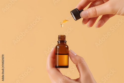Woman's hands holding dark serum or oil bottle and pipette isolated on empty beige background with space for text or inscriptions

