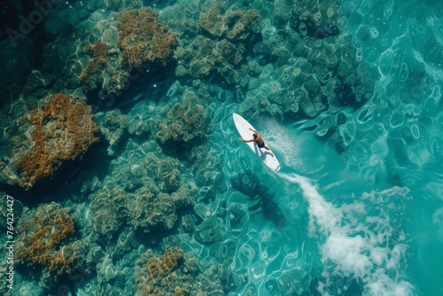 A person energetically rides a surfboard on the surface of a body of water, skillfully maneuvering the waves, Bird's-eye view of a surfer riding in a clear, coral-filled sea, AI Generated