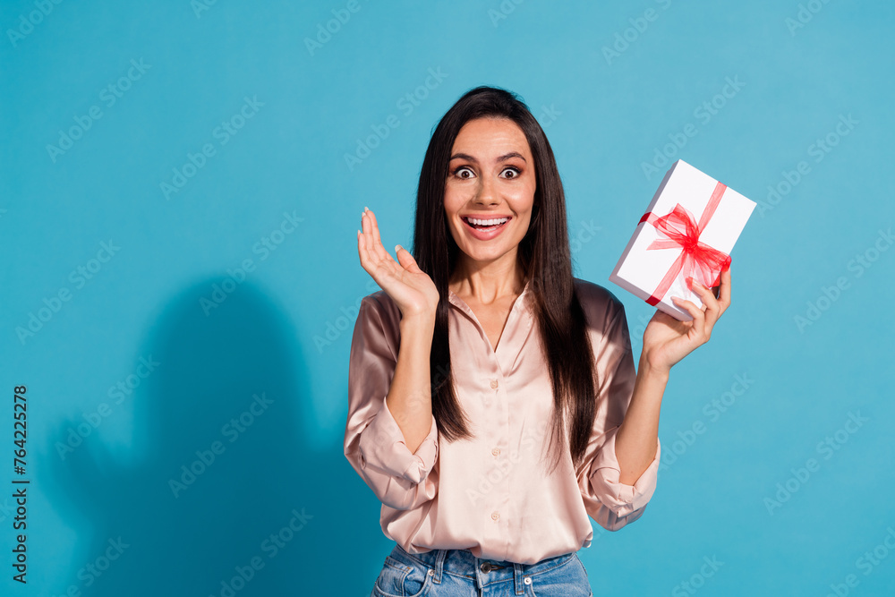 Photo of ecstatic crazy woman with straight hairdo dressed silk shirt holding present box in palm isolated on blue color background Photo of ecstatic crazy woman with straight hairdo dressed silk shirt holding present box in palm isolated on blue color background