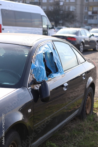 A car with a broken window is parked. A broken car window is covered with blue film.