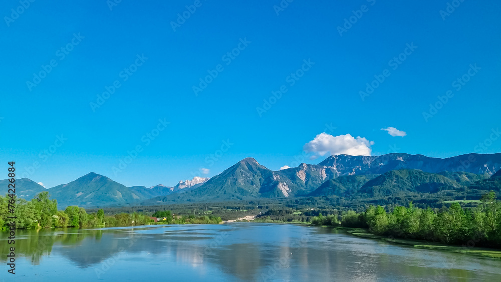 Drava river with panoramic view of majestic mountain ridges of Karawanks and Julian Alps, Carinthia, Austria, Europe. Idyllic landscape in Austrian Alps. Natural wilderness in summer. Wanderlust Drava river with panoramic view of majestic mountain ridges of Karawanks and Julian Alps, Carinthia, Austria, Europe. Idyllic landscape in Austrian Alps. Natural wilderness in summer. Wanderlust