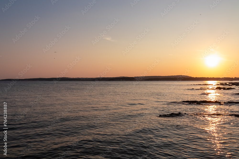 Beautiful sunset at rocky beach in coastal town Medulin, Istria peninsula, Croatia, Europe. Romantic view of rugged coastline Kvarner Gulf in Adriatic Mediterranean Sea in tranquil summer. Tranquility