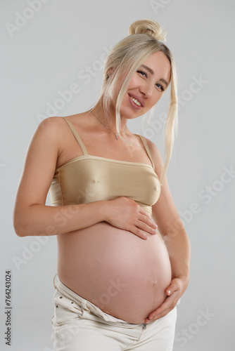 Tender portrait of a blonde pregnant woman isolated on a gray background. © ksi