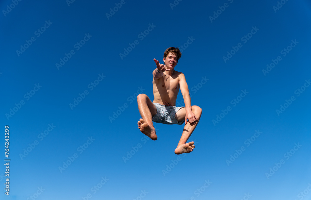 A young man in a swimsuit leaps into the air like Spider-Man against an intense blue sky, offering plenty of copy space. A young man in a swimsuit leaps into the air like Spider-Man against an intense blue sky, offering plenty of copy space.