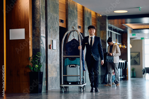 Hotel attendant pushing luggage cart in a lobby and looking at camera. photo