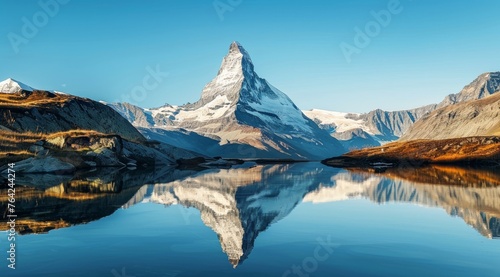 A mountain with a snow peak and a lake with a reflection of the mountain. The sky is blue and the mountains are covered in snow