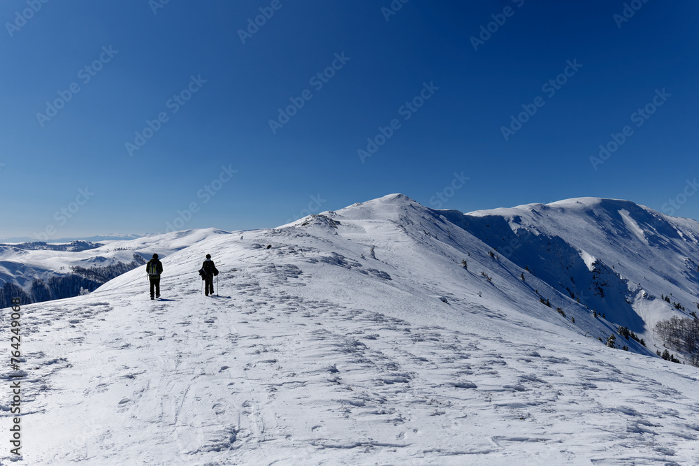 Two mountaineers walking towards the peak of the mountain. Beautiful sunny day for outdoor winter hike. Winter traveling. Adventure.