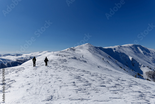 Two mountaineers walking towards the peak of the mountain. Beautiful sunny day for outdoor winter hike. Winter traveling. Adventure. © stu.dio