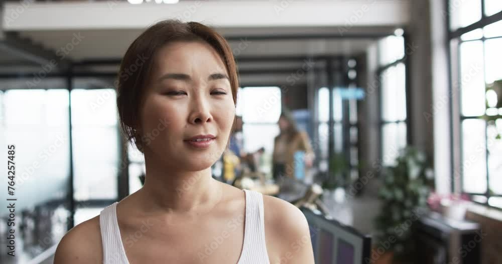 A middle-aged Asian woman stands confidently in a casual business office with copy space A middle-aged Asian woman stands confidently in a casual business office with copy space