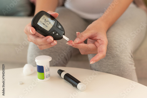 Close up of woman checking blood sugar level by using Digital Glucose meter, health care, medicine, diabetes, glycemia concept