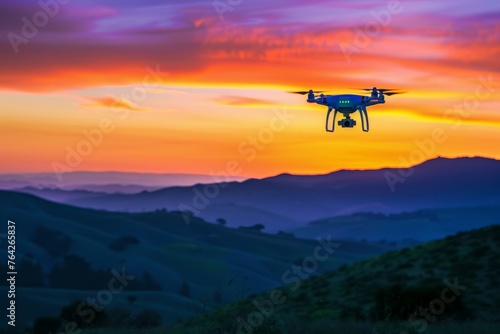 A small blue and yellow drone flies over a vibrant green hillside during twilight, silhouetted against the colorful sky