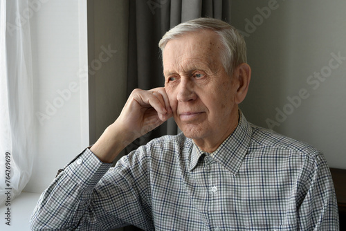 A pleasant elderly gentleman, 85 years of age, sits at home and looks thoughtfully out the window.