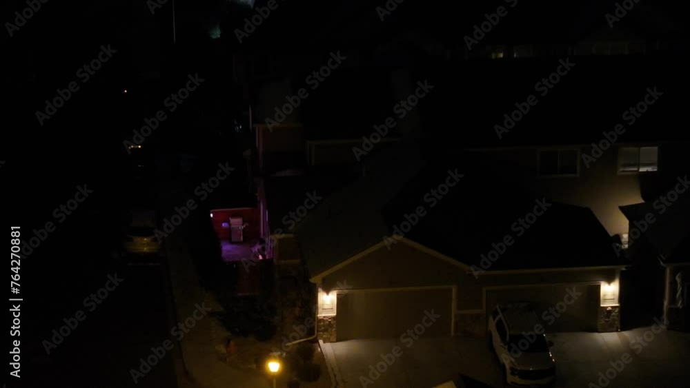 Aerial view at night of the side yard and patio of a condo with colorful landscape lighting and garage and condominium roofs partially covered with snow. Aerial view at night of the side yard and patio of a condo with colorful landscape lighting and garage and condominium roofs partially covered with snow.
